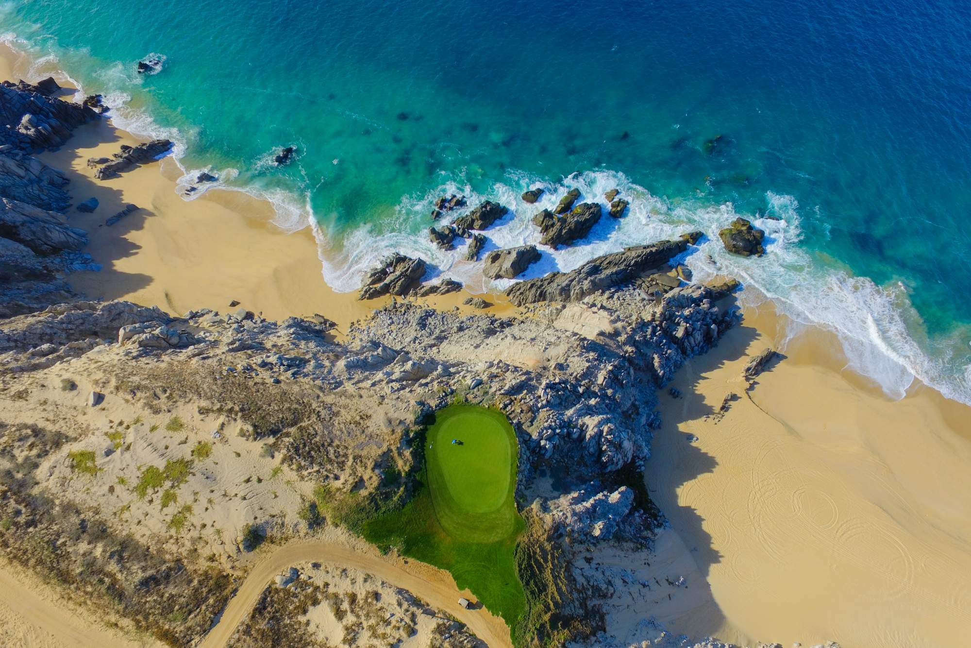 Aerial view of Quivira's iconic beachfront golf green with turquoise waters and golden sand