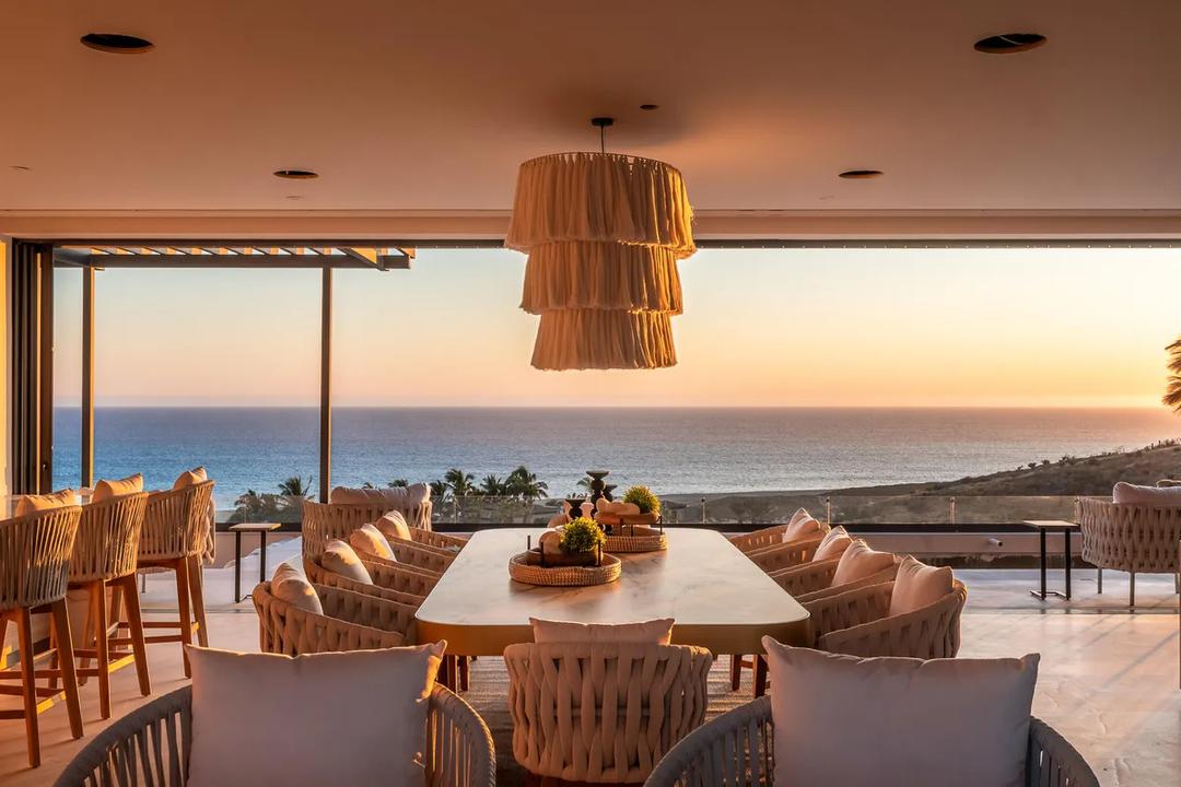 Elegant oceanfront dining area with panoramic sunset views, featuring sophisticated furnishings and dramatic pendant lighting