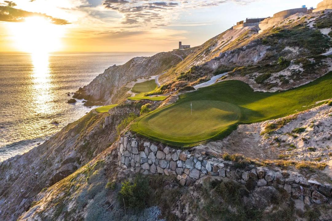 Dramatic sunset view of Quivira's signature oceanfront green with stone retaining walls and Pacific Ocean backdrop